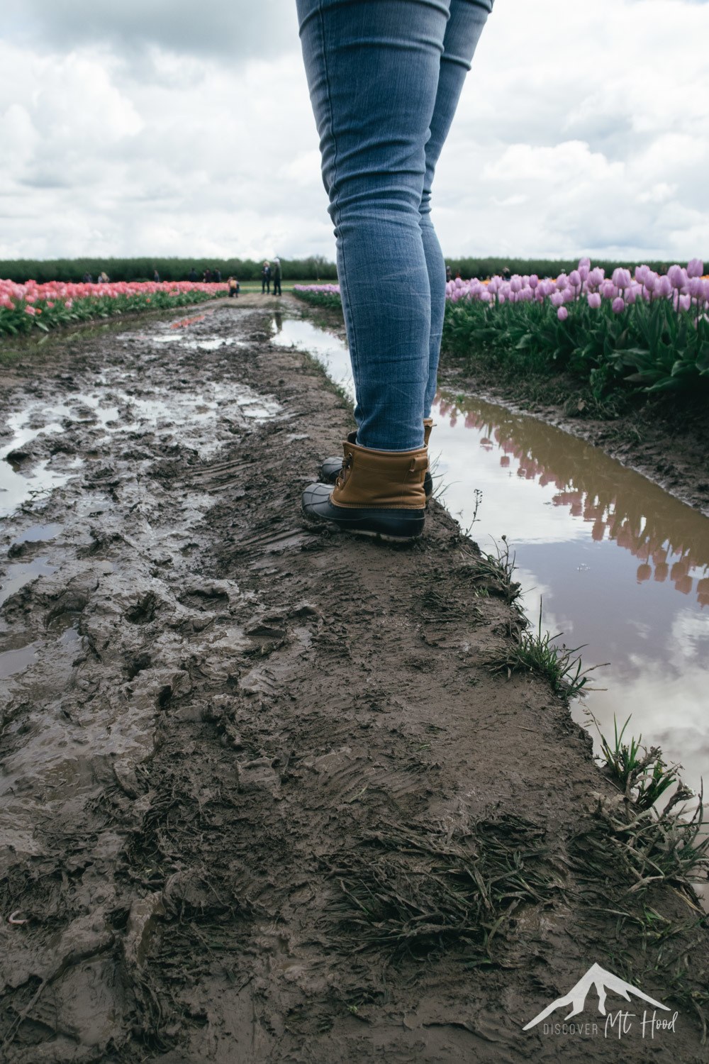 Girl wearing boots in mud while walking next to tulips